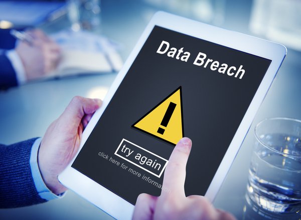 Person in suit and shirt holding a computer tablet with a data breach notification on the screen