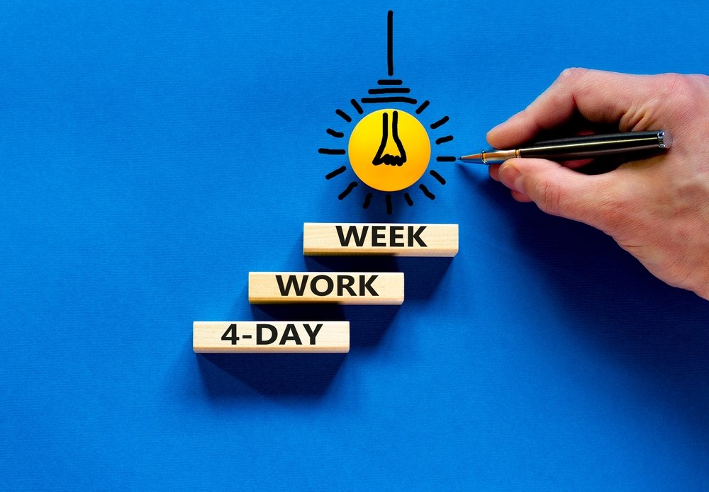 Blue background with a lightbulb drawn on it and four wooden shelves which say 4-Day Work Week